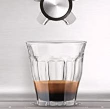 Glass sitting below a coffee machine spout 1/3 full.
