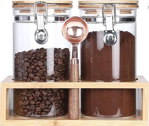 2 glass storage containers in a bamboo shelf with coffee in the jars and a spoon 