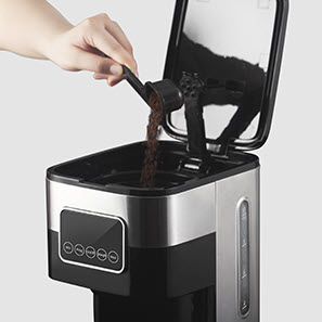 A lack scoop pouring coffee grinds into a coffee machine