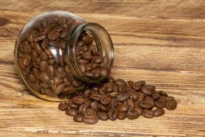 Coffee Beans in glass jar and spilled out, isolated on a wood grain background. Glass storage to keep Coffee Beans fresh.