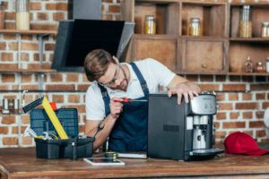 professional young worker in eyeglasses and protective workwear fixing coffee machine