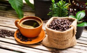 Hot Black Coffee in white cup with coffee beans in hemp sack on wooden table background