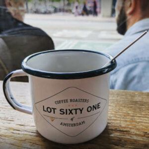 Black and white coffee mug with lot sixty one written in black text sitting on a wooden bench