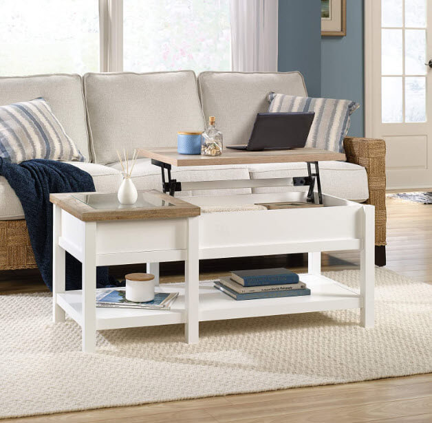 White lift up coffee table with a laptop on lifted section and a small white vase on the other section in a brightly lit living room 