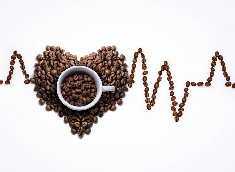 A white coffee cup surrounded by coffee beans in the shape of a heart