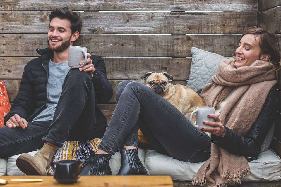 A relaxed couple sitting with their pug drinking coffee