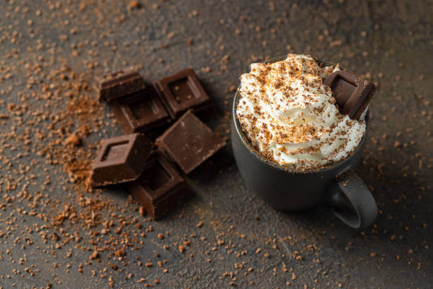 Hot chocolate cup with whipped cream and chocolate slices on dark concrete background. Warm cozy beverage for cold days