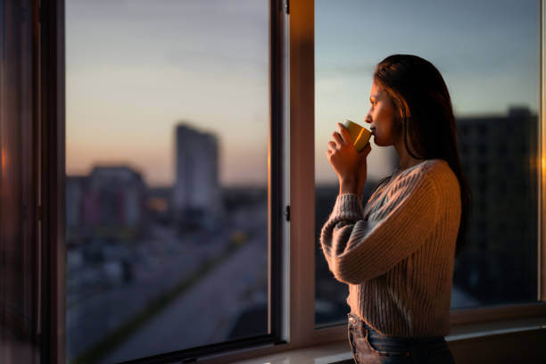 Young woman drinking coffee and day dreaming while looking through window.