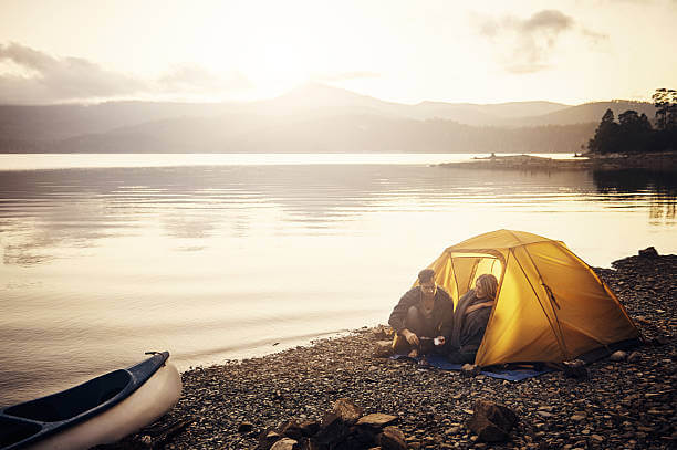 A couple sitting just outside their tent on a beautiful crisp morning by a lake.