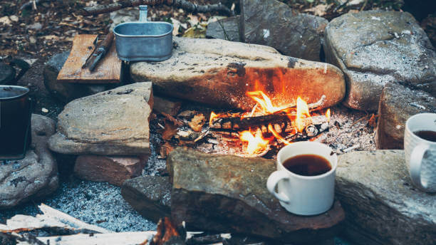 Hot coffee or tea in mugs near campfire.