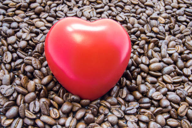 Figure heart is among roasted coffee beans. Effects of coffee and caffeine on heart function, heartbeat, rhythm, and role in development of heartburn, attack, arrhythmia, failure and other diseases