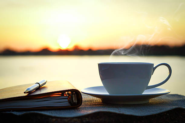 Silhouettes of sunrise morning coffee with a note and a pen