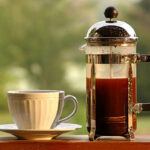 A french press with a small white coffe cup