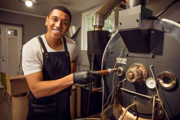 Smiling pleased African American roast master holding the roasted Arabica beans in the sample spoon