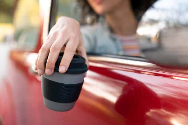 Young woman driving through Argentina on a Road Trip. Here using a travel mug in the car, holding in out the window.