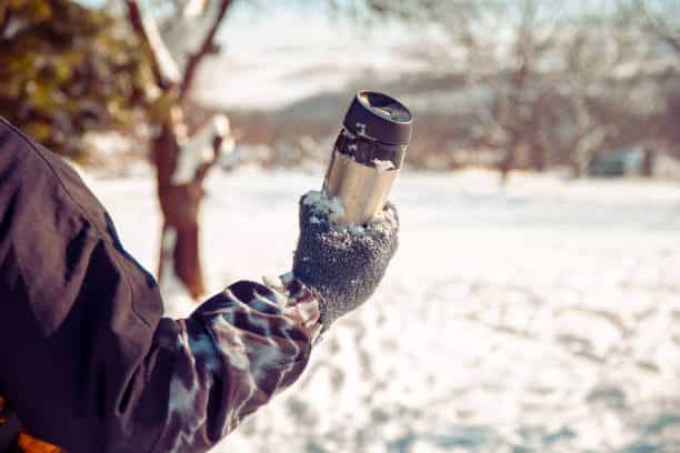 Man holding Thermos with hot Drink Outdoors on Winter hiking. Warming and refeshing with tea or coffee on cold day
