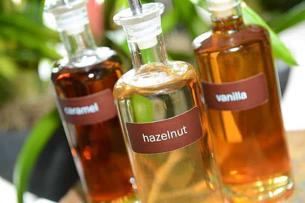 Pretty glass bottles containing hazelnut, vanilla and caramel coffee syrups for flavoring a drink.