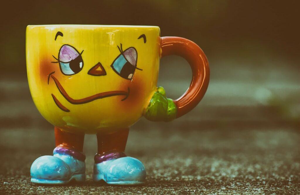 A comic looking mug with a clown like face legs and a hand as the mug handle.