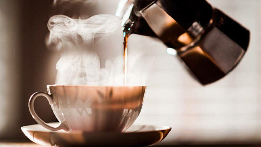 Coffee being poured into a coffee cup from Espresso Maker with beautiful steam in the morning light.