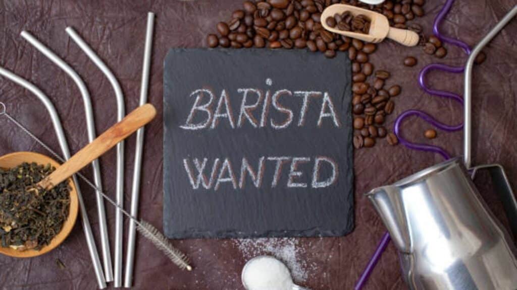 barista wanted written with chalk on a black stone tile, surrounded by coffee, tea, sugar and bartender utensils