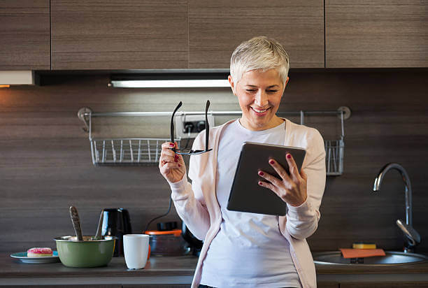 Mature woman using digital tablet at kitchen, looking for recipe on internet