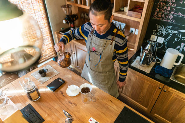 High angle view of mature Chinese man making pour-over coffee in cafeteria