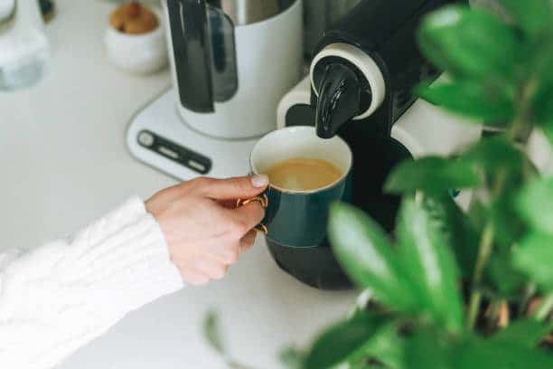 Crop photo of young woman pours coffee from coffee machine in kitchen at home