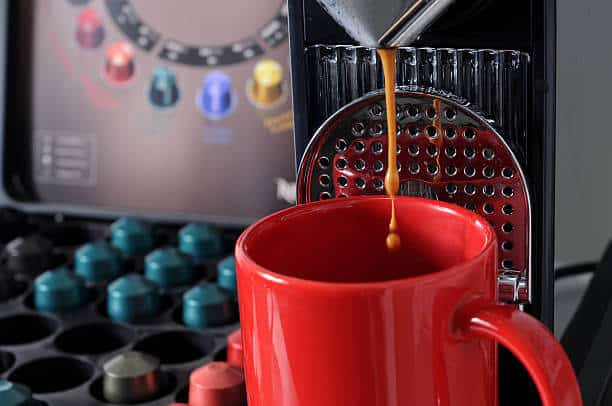Nespresso coffee pod machine making coffee with red mug and various Nespresso capsules at the background