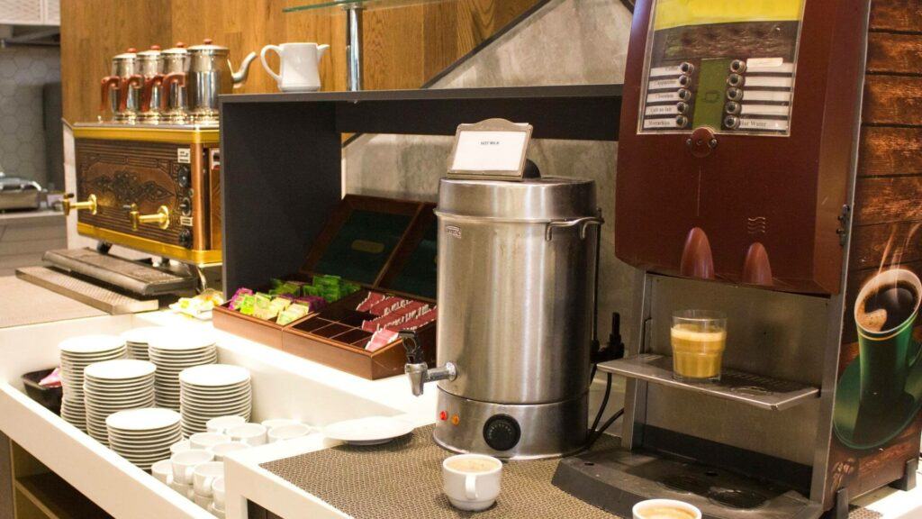 A coffee station with all types of coffee accessories including a coffee maker and large stainless steel coffee urn.