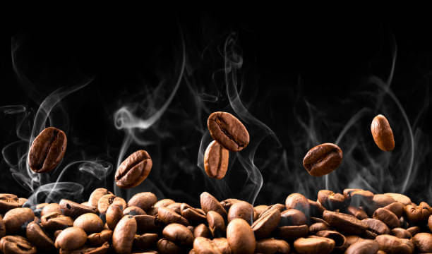 Coffee beans fall in smoke on a black background.