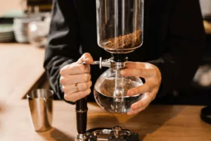 Barista is holding siphon before starting boiling water inside syphon. Process of brewing siphon coffee in cafe