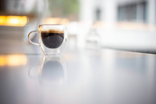 A glass coffee cup filled with black coffee against a blurred background.