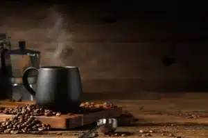 Cup of coffee with smoke and coffee beans on old wooden background. Moka pot and coffee cup. Moka pot and coffee cup