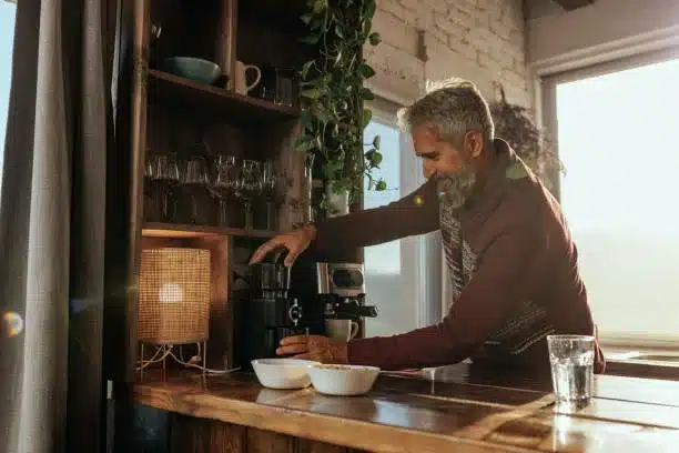 A senior Caucasian man is making himself a cup of coffee at home on his small espresso machine.