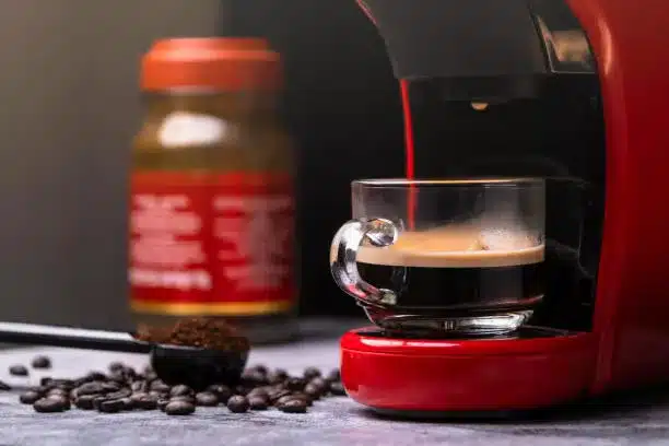 Hot coffee flows into a cup with an espresso machine, close-up. Modern espresso machine with ground coffee grounds in a spoon and coffee beans spilled around on wood table.