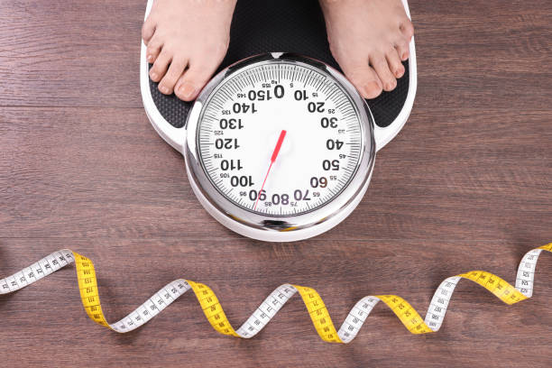 Closeup of woman using scales on floor near measuring tape, top view. Overweight problem