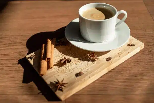 Breakfast in a cafe with a cup of coffee, on a bamboo board sprinkled with cane sugar, with anise and cinnamon sticks. Brown colors, warm autumn day