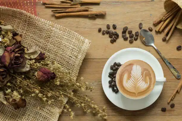 Cup of latte art or cappuccino coffee with dried flower on wooden table showing the health benefits of cinnamon coffee.