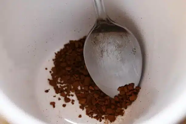 a spoonful of instant coffee granules in the bottom of a white mug with old tarnished silver spoon
