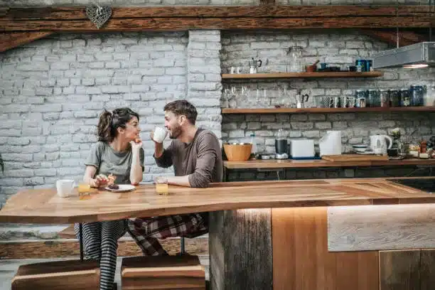 Happy couple in pajamas talking to each other during their morning coffee in the kitchen.