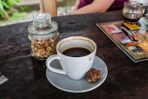 A cup of Kopi Luwak Coffee in a white cup sitting on a dark brown wooden table.