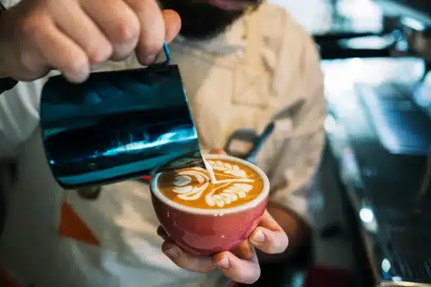 Professional barista pouring steamed milk into coffee cup making beautiful latte art.
