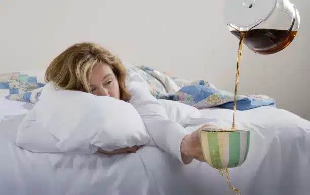 Exhausted woman in bed wanting more coffee.